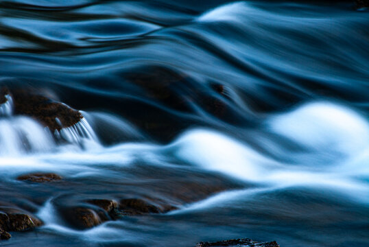 Flowing water over rocks in Iceland with smooth long exposure effect. Peaceful Iceland nature scene with blue tones, soft motion, and detailed texture of river and stones.
