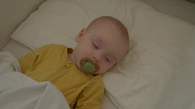 caucasian baby sleeping beside pacifier, dreaming sleeper in yellow onesie on soft pillow with gentle nightlight glow, serene nap routine, tranquil nursery ambiance