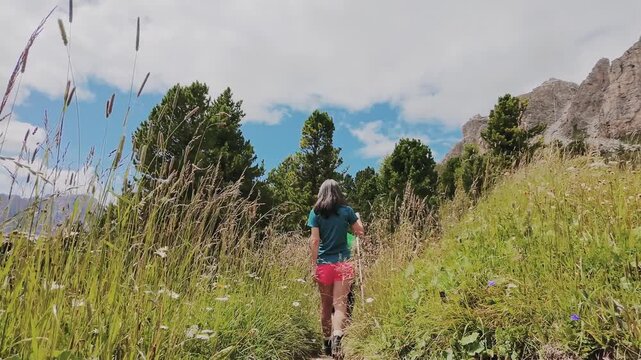 fClose up tracking view couple treks through lush meadows forest in famous summer destination Dolomites. Active lifestyle weekend get away trek in Europe summer holidays