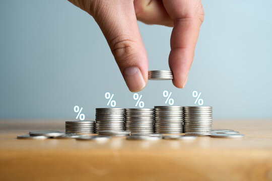 Hand stacking coins with percentage icons representing rising interest rates and profit