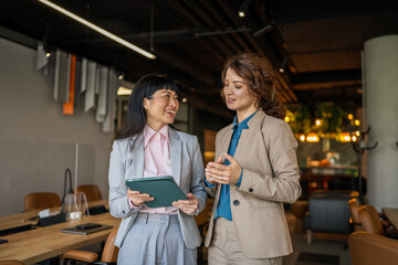 Diverse businesswomen collaborating on digital tablet in modern office