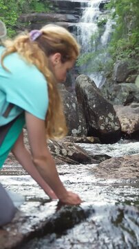 Young woman drinking fresh water from a clean forest stream in summer. Pure nature, peace, and refreshment. A quiet moment in the wilderness, symbol of connection with nature and natural living.