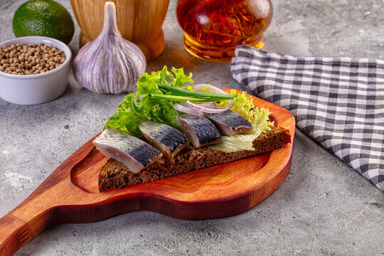 Pickled herring appetizer on rye bread with lettuce, onion, and garlic on a wooden board