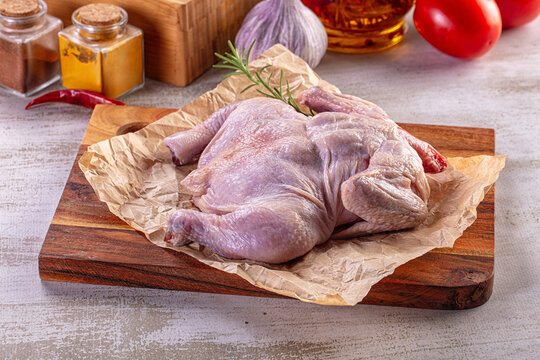 Raw whole chicken on a wooden cutting board with fresh herbs, spices, and vegetables.