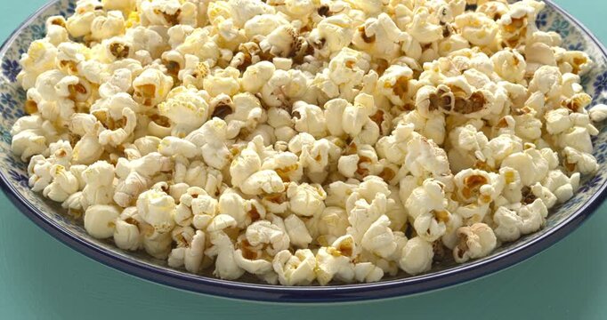 Freshly made popcorn on a plate, blue background, table spin.