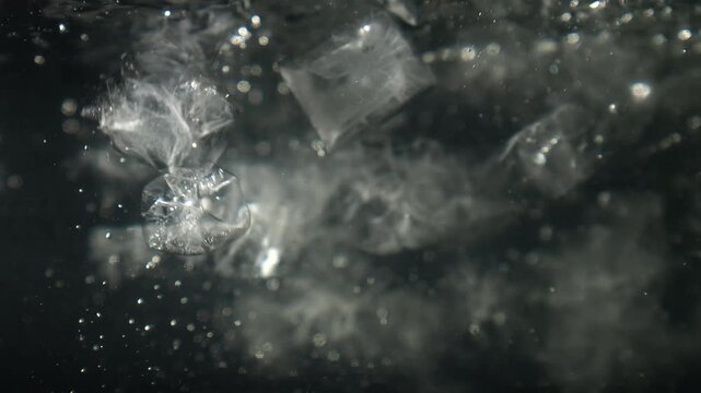 Ice cubes falling into water with oxygen bubbles, frost patterns, and soft light reflections. Concepts for beauty advertising, menu designs for bars and restaurants, cryotherapy.