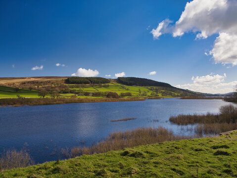 Bright view of Gouthwaite Reservoir in Yorkshire UK with blue water rolling hills and scattered clouds in crisp spring light