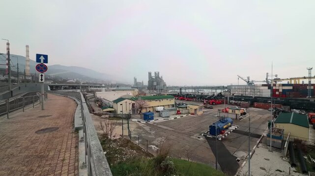 Industrial panoramic view of Novorossiysk commercial sea port at Black Sea coast with red reach stackers freight train wagons container terminals and massive grain silo under overcast sky daytime