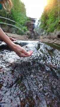 Young woman drinking fresh water from a clean forest stream in summer. Pure nature, peace, and refreshment. A quiet moment in the wilderness, symbol of connection with nature and natural living.