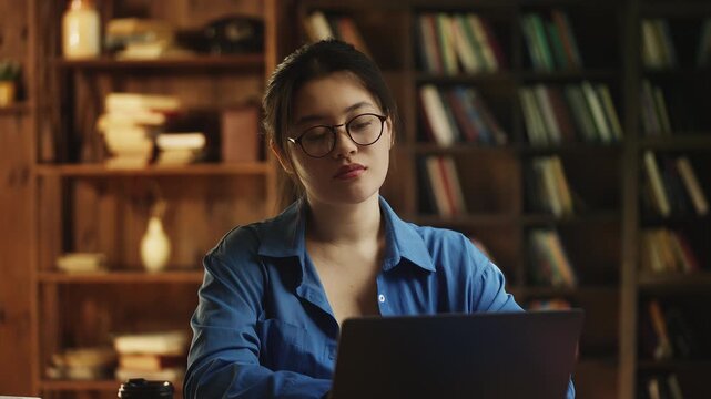 Young Korean woman in eyeglasses working on laptop in public library, freelance