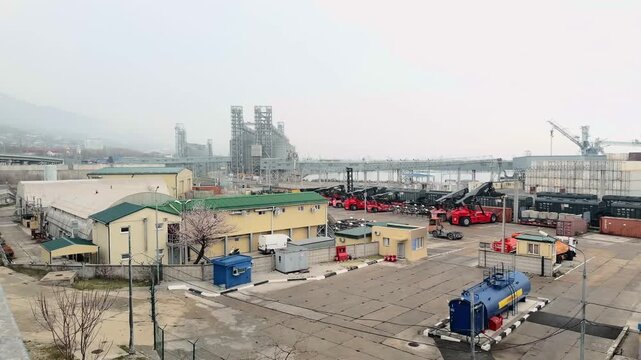 Wide 180 degree panoramic view of Novorossiysk commercial sea port industrial zone with red reach stackers container terminal and massive grey grain silo complex at Black Sea coast overcast day