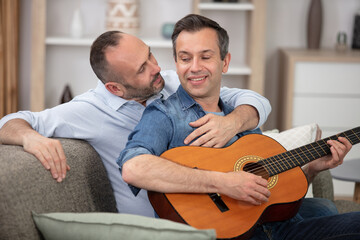 Fototapeta premium gay couple with guitar sitting on sofa at home