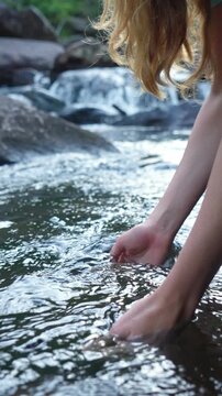 Young woman drinking fresh water from a clean forest stream in summer. Pure nature, peace, and refreshment. A quiet moment in the wilderness, symbol of connection with nature and natural living.