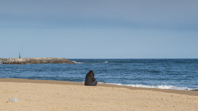 Mujer sola sentada frente al mar en la playa.