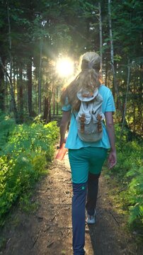 Woman with backpack walking on sunlit forest path in Norway. Authentic lifestyle, mental health wellness and sustainable solo travel concept in Northern Europe.