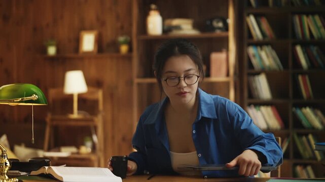 Young Asian woman drinking coffee and beginning her work on laptop in library