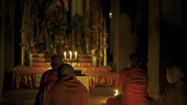 Young Buddhist monks sitting in meditation during a religious ceremony inside a dark temple
