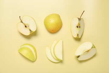 Cut fresh apples on pale yellow background, flat lay