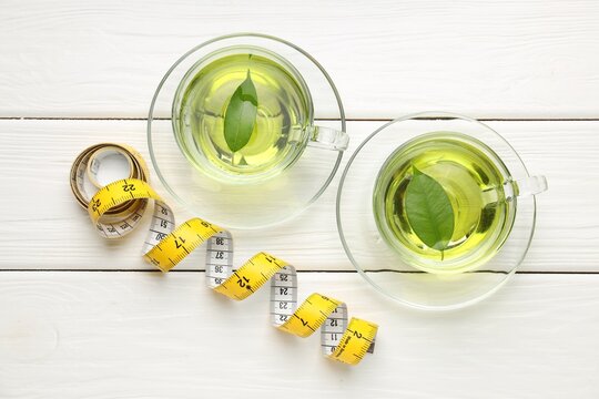 Weight loss tea and measuring tape on white wooden table, flat lay