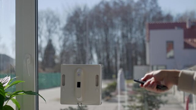 Woman presses stop with remote control and window cleaning robot stops on window. Concept of smart home control and automated cleaning