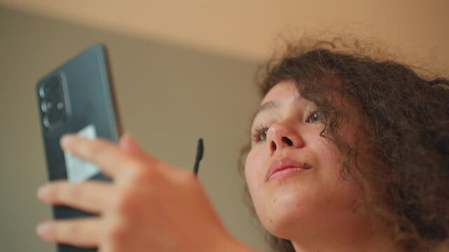 Woman applying makeup. Beauty enthusiast preparing for evening. Woman confidently applying mascara in hotel room setting. Female personal grooming routine captured during beauty tutorial session