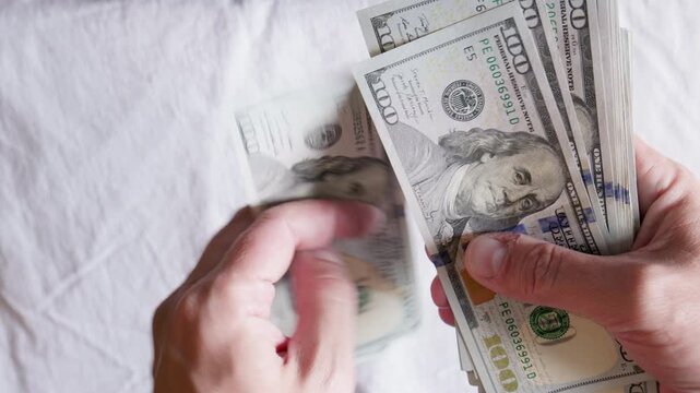 Blurred hands skillfully count a stack of US dollar bills on a textured white surface. Scene evokes feelings of wealth, abundance, and financial transactions.