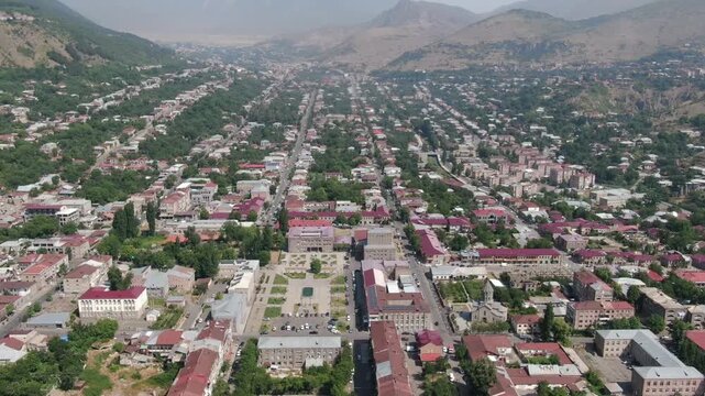Beautiful aerial drone view of Goris, a picturesque city nestled in a green valley surrounded by majestic mountains in Armenia, featuring a long main street and red roofs.