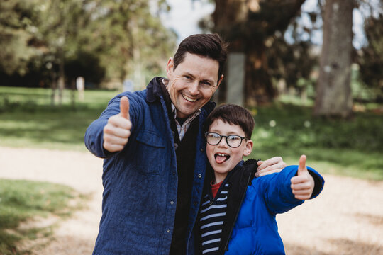 Father and son showing thumbs up smiling together outdoors in park