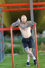 Fototapeta premium Tattooed man giving thumbs-up at outdoor gym