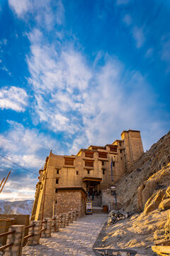 Majestic view of the historic Leh Palace bathed in golden sunlight against a vibrant blue sky with wispy clouds, a popular tourist landmark in Ladakh, India 