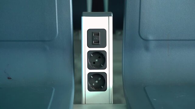 Power outlet station with USB ports placed between seats, providing convenient device charging in a modern public space or transport setting.