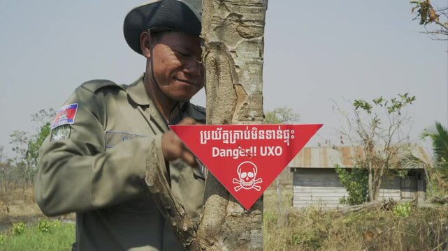 Demining expert placing a red triangular warning sign for unexploded ordnance - UXO - in Cambodia