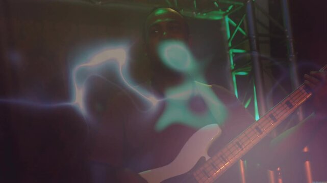 Bassist playing white bass on stage, projection sweeping while light streak showing neck in concert