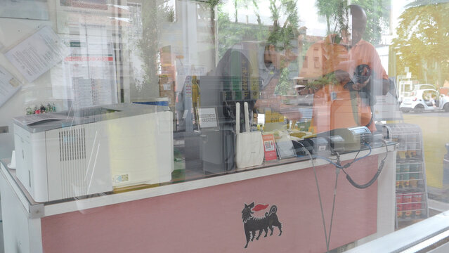 A service station employee is visible behind the counter, surrounded by payment devices and various goods for sale