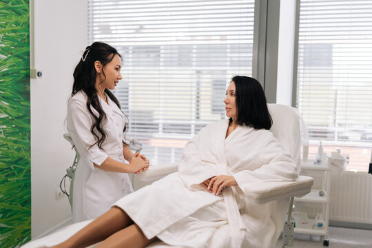 Side view of Asian beauty expert engaging in consultation about cosmetic treatment with woman in chair at aesthetic clinic, elaborating on specifics of procedure. Concept of facial anti-aging.