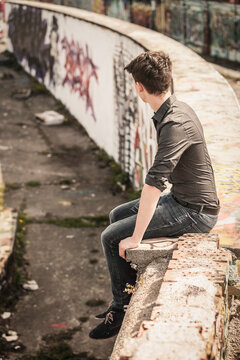 Young Man Sitting on a Graffiti-Covered Concrete Wall