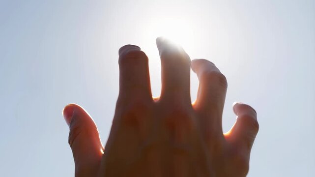 Hand reaching towards the sun against a clear sky. Symbolizes hope, aspiration, and the pursuit of dreams
