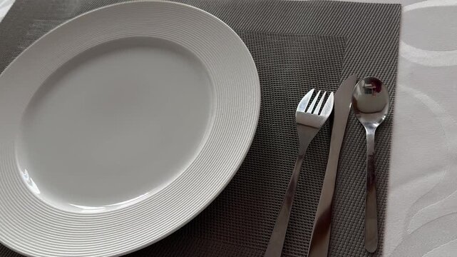 White empty plate fork knife spoon on dark gray placemat dining setup