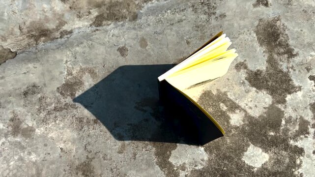 Small book with turning pages casting a sharp cinematic shadow on a rustic surface in high angle shot