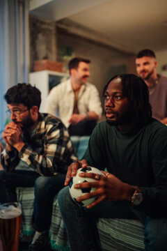 Diverse friends eagerly watching football match at home together, celebrating sport and teamwork