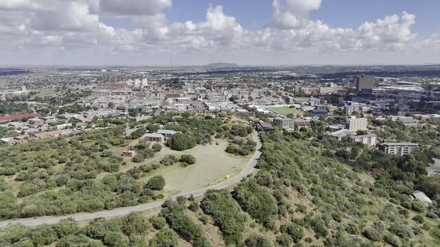 Drone flies southwest over Naval Hill and over Mandela statue overlooking city on partially cloudy afternoon in Bloemfontein, South Africa