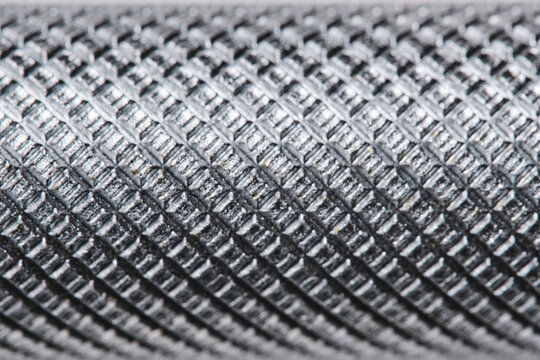 Extreme macro texture metal tool handle with knurled diamond pattern, showing industrial detail and steel surface.