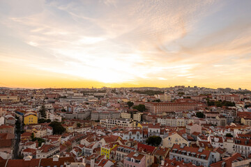Fototapeta premium Aerial-style elevated view overlooking the historic city of Lisbon, Portugal, with colorful buildings, terracotta rooftops, and the Tagus River stretching across the horizon at sunset