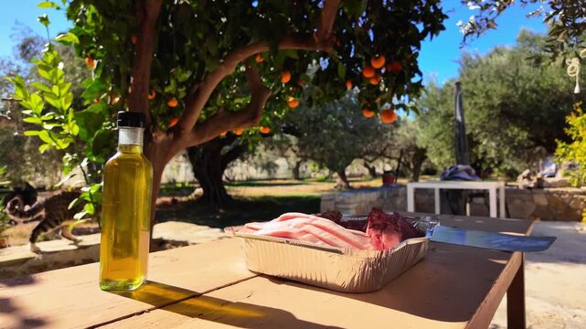 4K slow-motion shot of pork chops cooking outdoors under an orange tree, with olive oil foreground for a natural, rustic Mediterranean food scene.