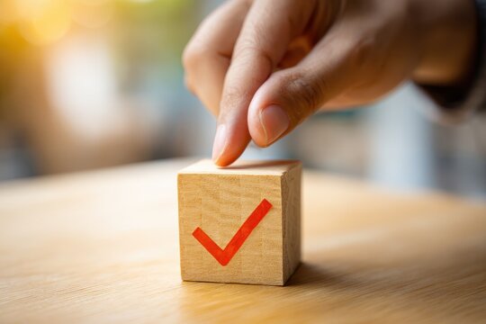 Wooden cube with a bold red tick being added by a fingertip for a task planning concept