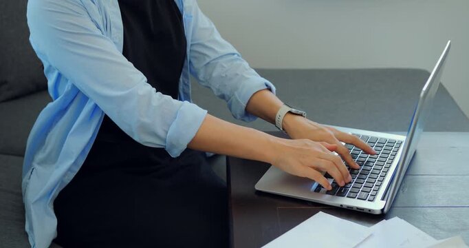 Relaxed person working from couch. Freelancer engaged in report writing at home. Person comfortably seated on sofa multitasking while preparing documents and joining online discussions