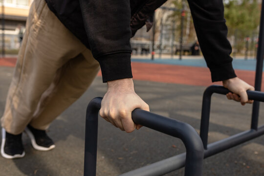 Man doing push ups on parallel bars at outdoor gym close up. 