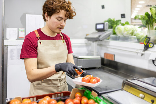 Shop assistant arranging fresh tomatoes at grocery store