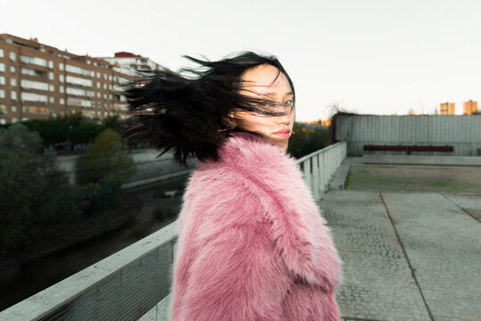 Asian woman in pink fur coat on urban rooftop