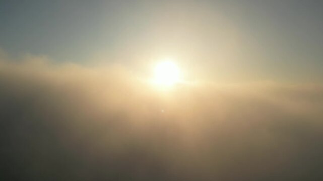 Cinematic aerial tilt down shot descending through thick fog and clouds to reveal the top of the historical White Tower in Thessaloniki, Greece at sunrise.